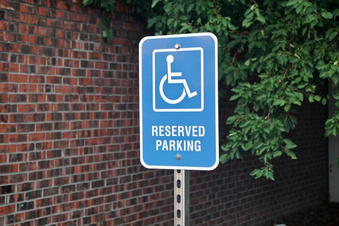A blue reserved parking sign for disabled individuals next to a brick wall