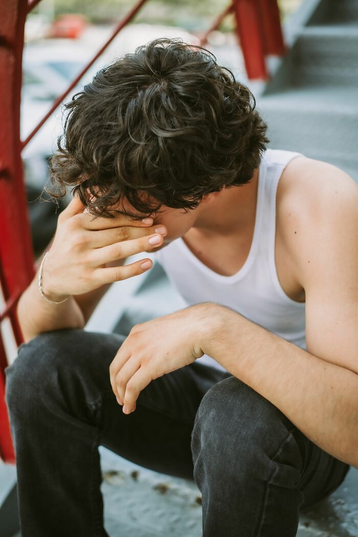 A young man with curly hair covering his face with his hand, showing the emotional challenges children experience.