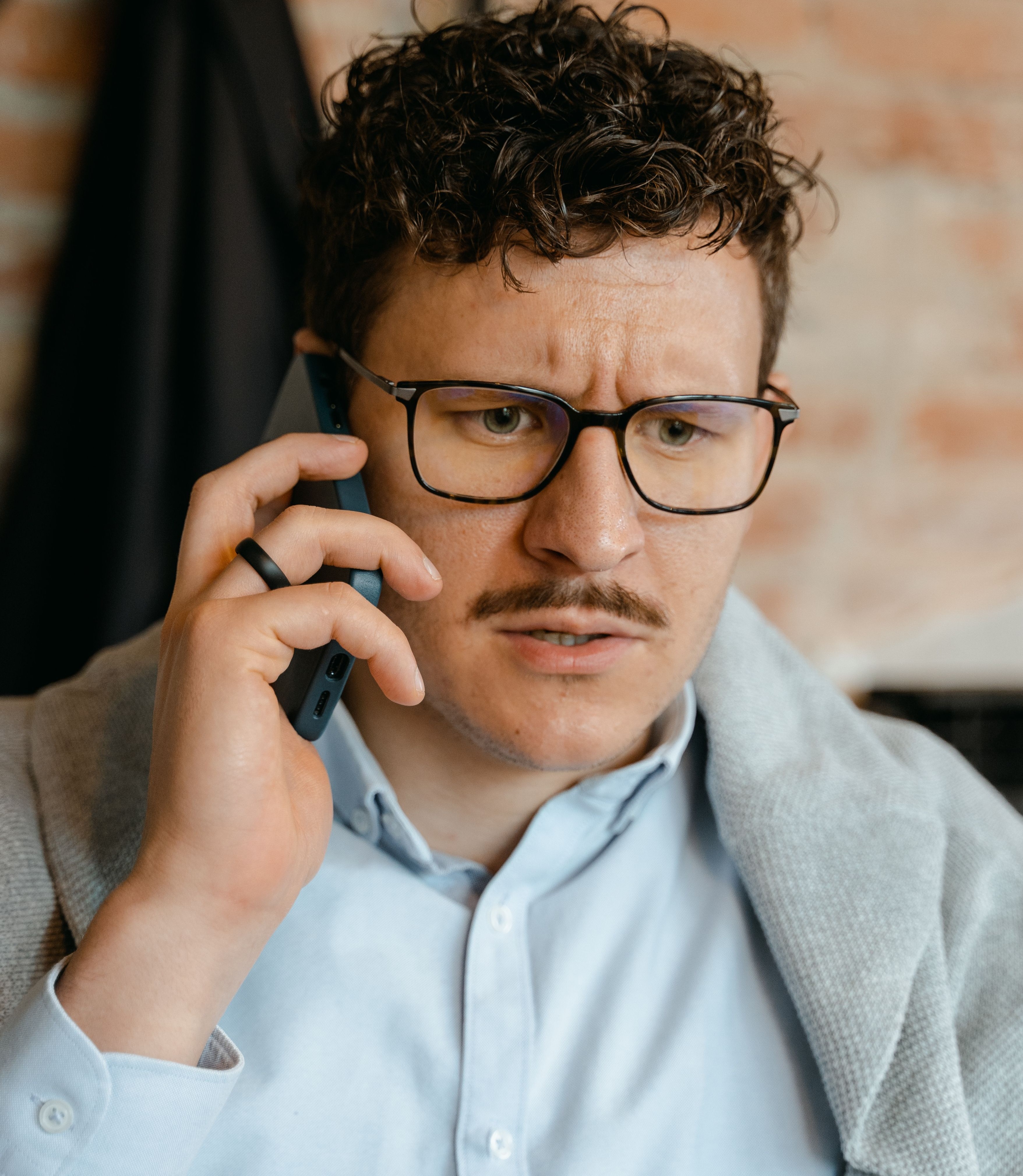 A close up photo of a man on the phone looking concerned after being a victim of a credit card thief