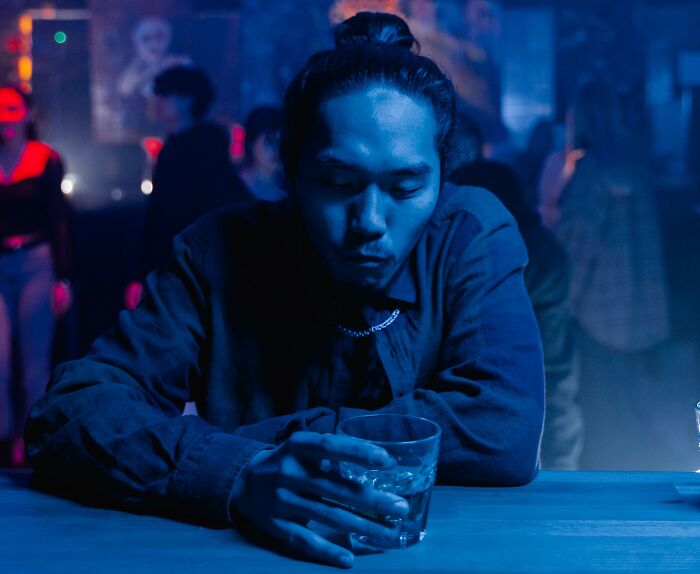 A man looking down thoughtfully at a bar with a drink, reflecting on having money