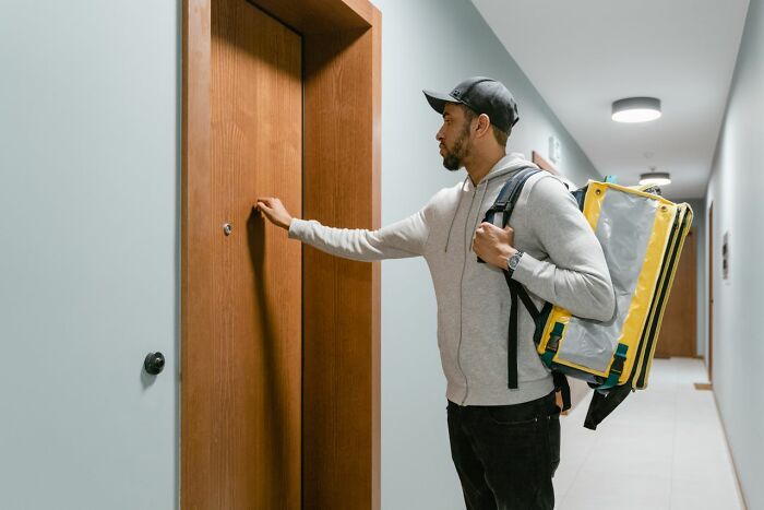 A delivery man knocking on a door, highlighting safety tips for women living alone regarding deliveries.