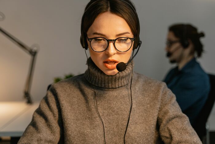 A woman wearing glasses and a headset speaks at her desk, avoiding any scandals.