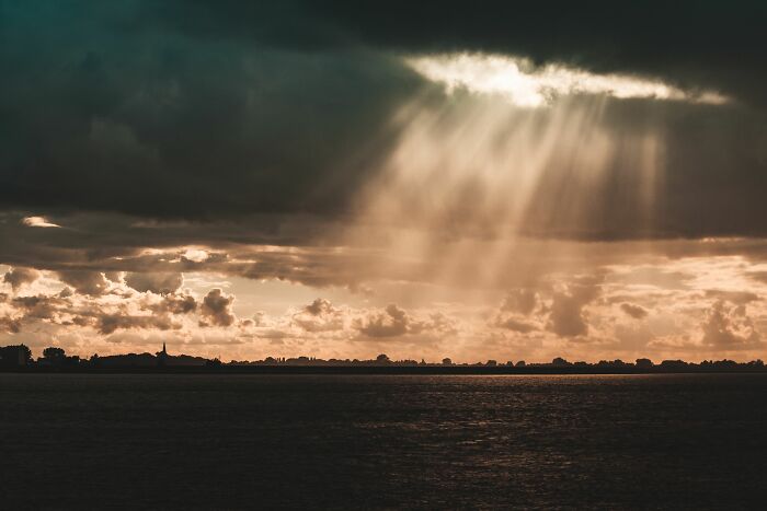 Sun rays piercing through dark clouds over a body of water, symbolizing childhood beliefs.