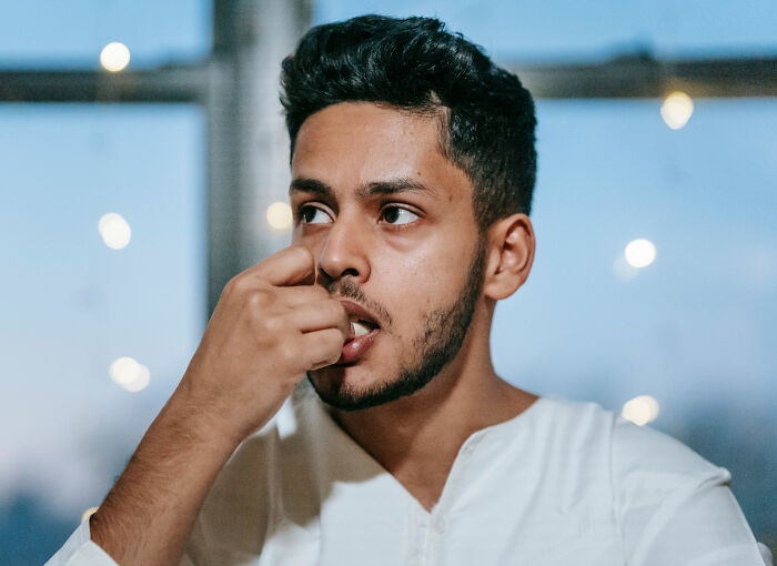 A man with a beard bites his fingernails, appearing anxious, relating to innocent health symptoms that terrify doctors.