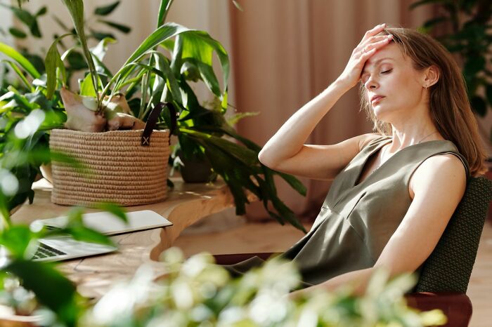 An exhausted woman holding her forehead at her desk, experiencing fatigue as part of body changes in her 30s.