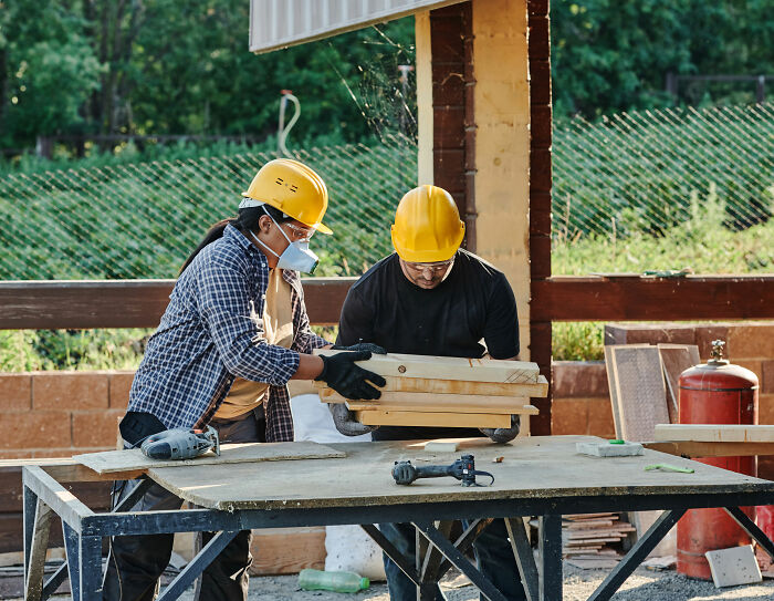 Two fence builders working, wearing hard hats and safety masks, constructing or deconstructing a fence. Two fence builders working, wearing hard hats and safety masks, constructing or deconstructing a fence.