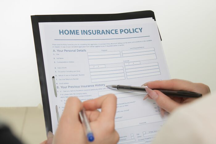 Hands holding a pen over a Home Insurance Policy document, pointing to potential insurance scandals.