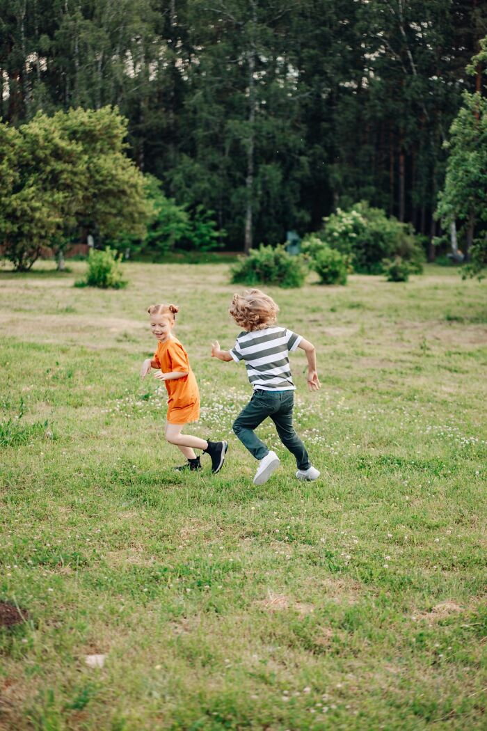 Two happy children running and playing in a grassy field, depicting simple joys of childhood.