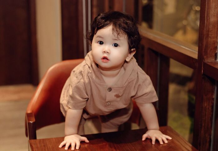 A cute baby of rich people sitting on a high wooden chair