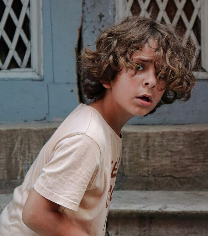 A young boy with curly hair looking shocked or surprised, demonstrating someone who overheard a secret.