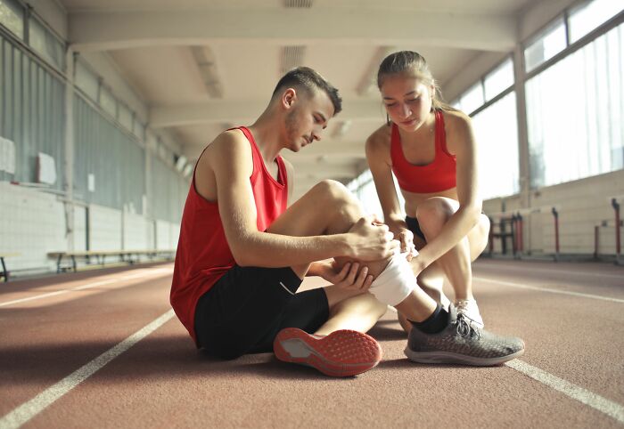 A woman bandaging a man's leg, demonstrating a pain reaction to a sports injury.