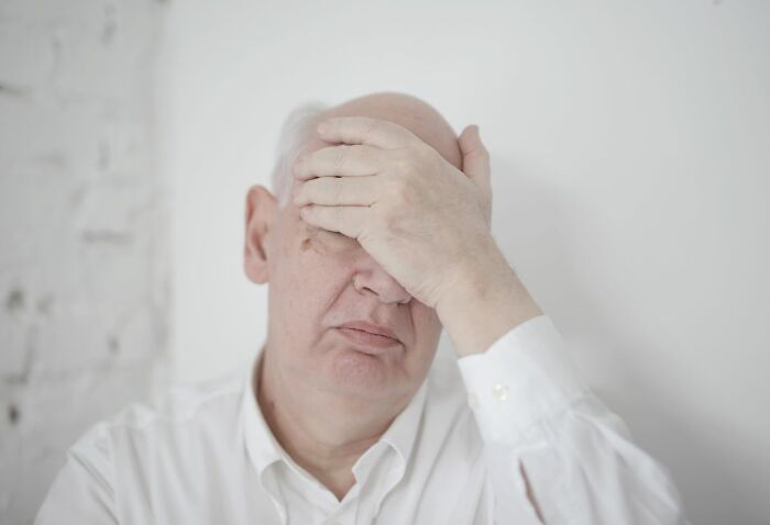 An elderly man with his hand on his face, feeling judged for a petty action.