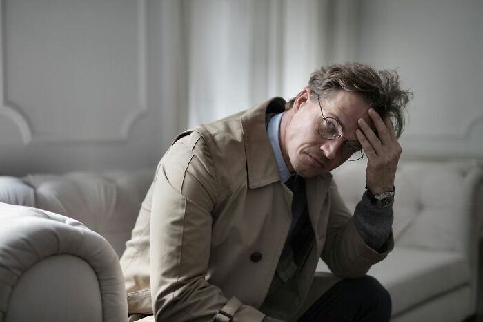 Stressed man holding his head, experiencing a lack of simple joys no longer pleasurable due to mainstream culture.