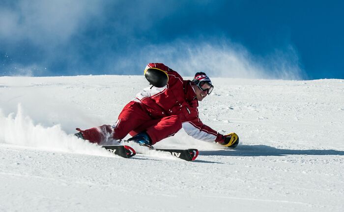 A skier in red, leaning into a turn on a snowy slope, possibly reacting to a pain.