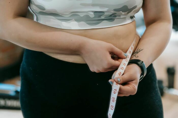 A person measuring their waistline with a tape measure, experiencing body changes after turning 30