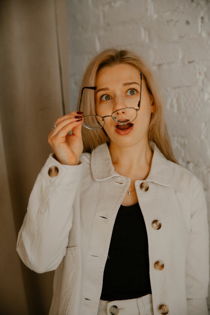 A woman holding glasses and looking surprised, representing people who overheard something they werent meant to hear.