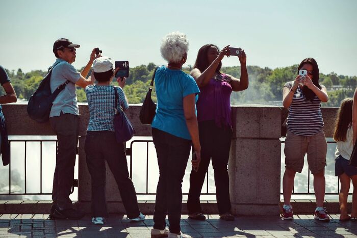 Tourists capturing photos with their phones, showing how mainstream photography impacts simple joys.