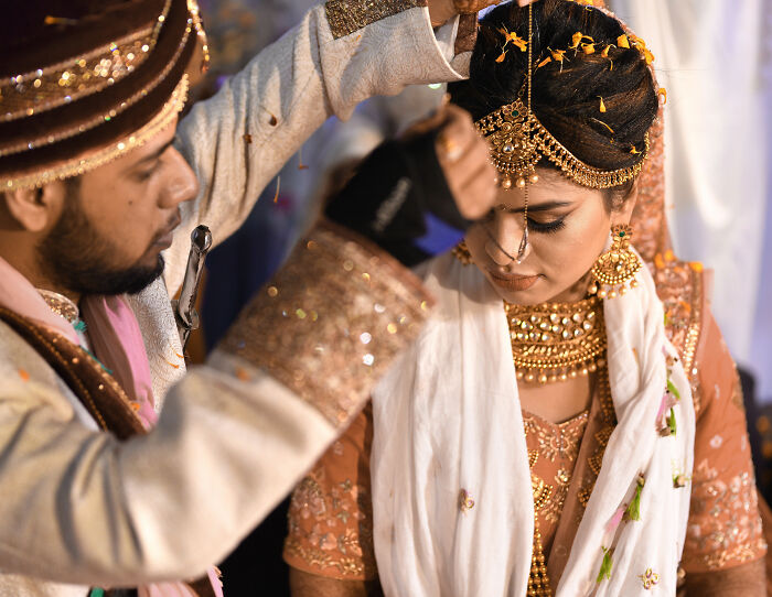 A man adorning a woman during her wedding day, highlighting the traditional rituals and cultural implications. A man adorning a woman during her wedding day, highlighting the traditional rituals and cultural implications.