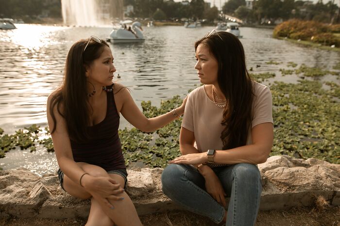 Two women having a serious conversation by a lake, representing people overheard interactions.