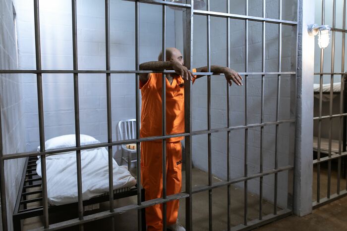 A man in an orange jumpsuit behind bars, conveying how therapists find a sociopath.