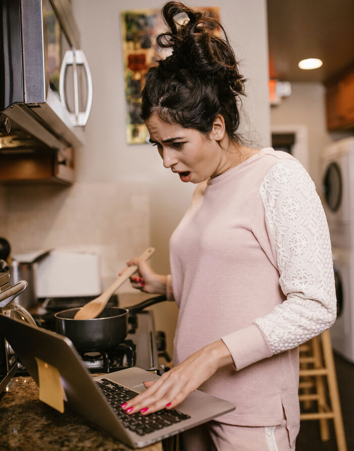 A woman looking shocked while cooking and looking at a laptop, possibly due to crazy lies men told them.