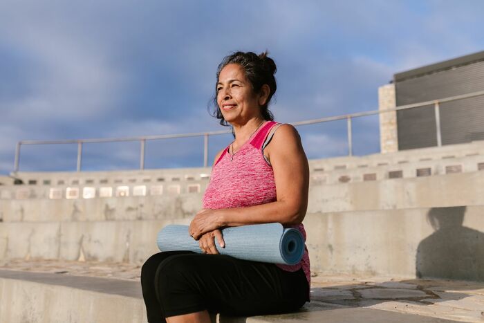 A woman smiling outdoors holding a yoga mat, showcasing positive body changes and healthy aging