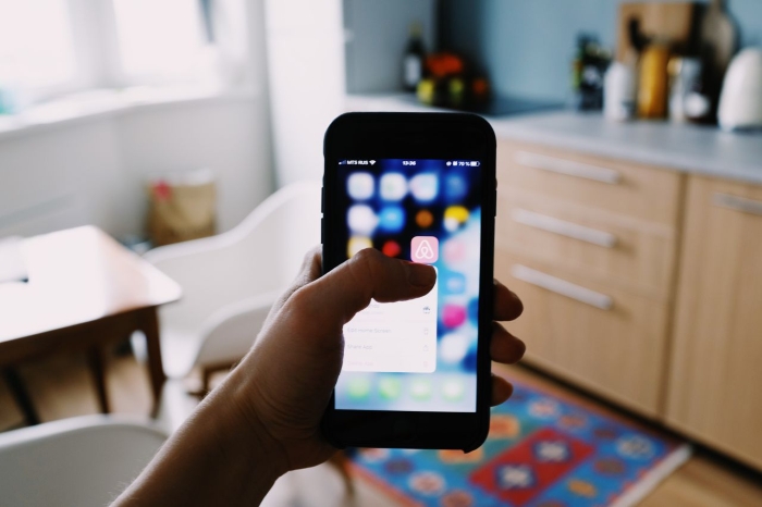 A hand holding a smartphone with the Airbnb app icon on screen, representing a man's experience with his Airbnb stay. A hand holding a smartphone with the Airbnb app icon on screen, representing a man's experience with his Airbnb stay.