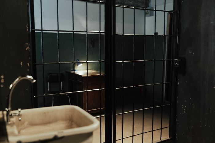 A view through prison bars into an interrogation room, symbolizing secrets that came to light.