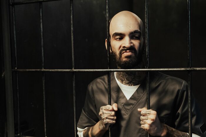 A man with tattoos behind prison bars, representing the consequences of a sociopath's actions.