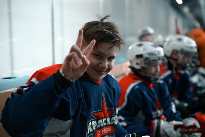 A young ice hockey player showing a peace sign, surprisingly dealing with pain reactions.