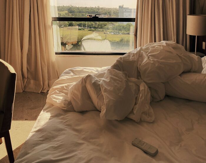 An unmade bed with white linens in a bright room, highlighting rich people living spaces