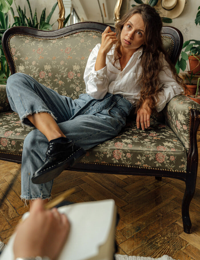 A female client sitting on a patterned sofa, possibly a sociopath, in a therapy session.