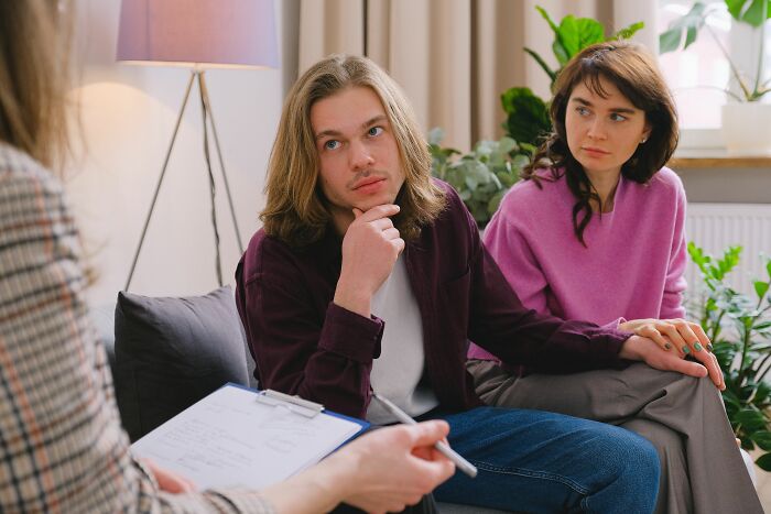 A couple in therapy, with the man potentially being a sociopath, listening intently to the therapist.