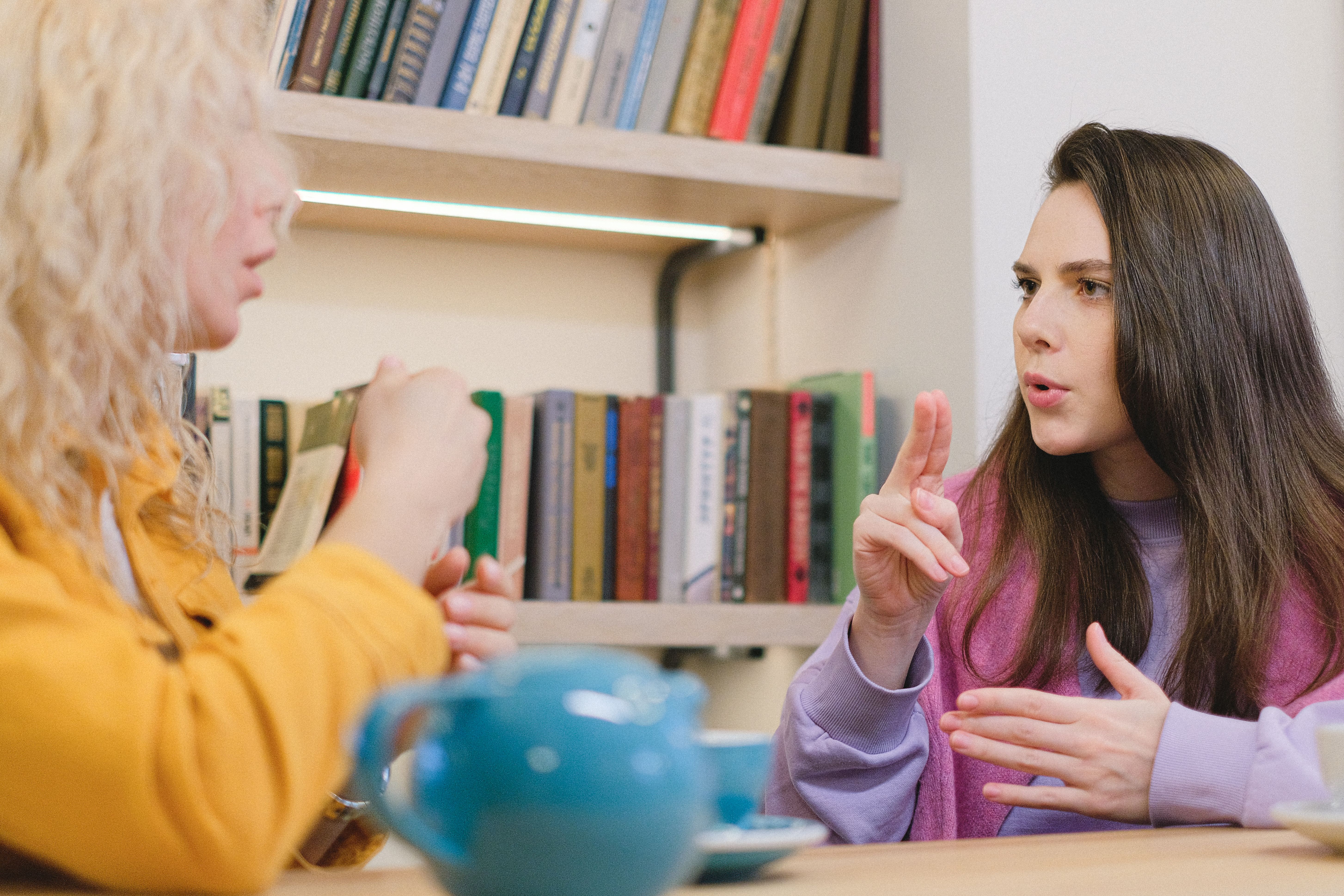 Two women communicating using sign language in a room with books Two women communicating using sign language in a room with books