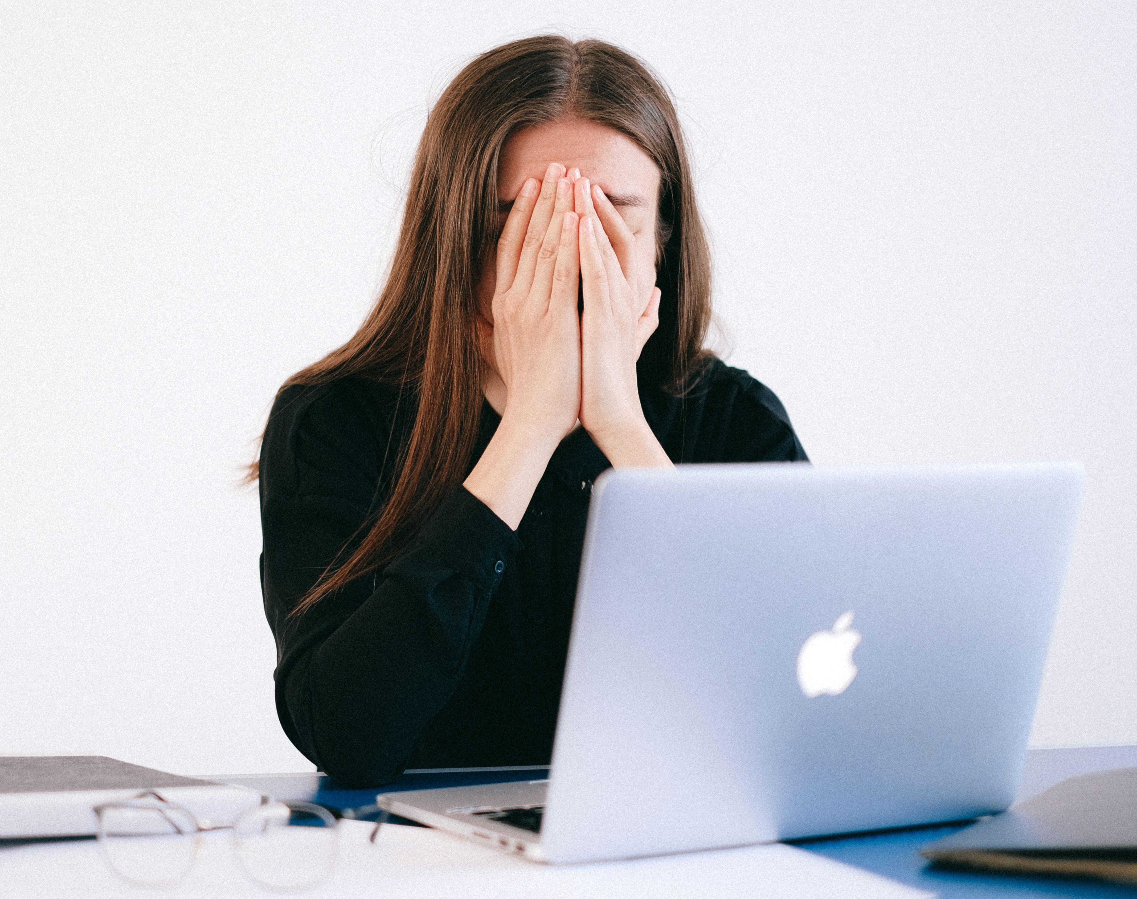 A woman covering her face in stress while sitting at a laptop, dealing with a potential gender-biased situation A woman covering her face in stress while sitting at a laptop, dealing with a potential gender-biased situation