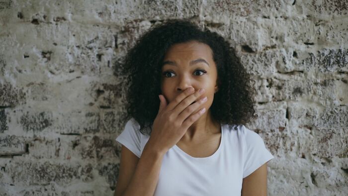 A woman with curly hair looking surprised, covering her mouth with her hand, enjoying a delicious dinner at a restaurant.