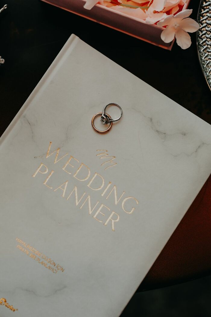 Wedding planner book with rings, hinting at future celebrations and delicious dinner, or hot tea from a table nearby.