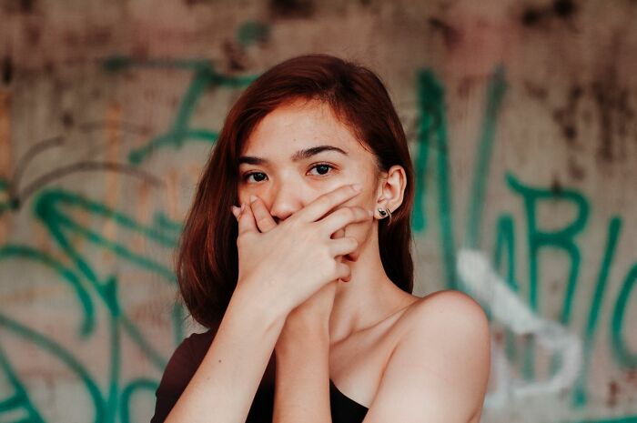A woman covering her mouth, looking at the camera, waiting for hot tea from a nearby table.