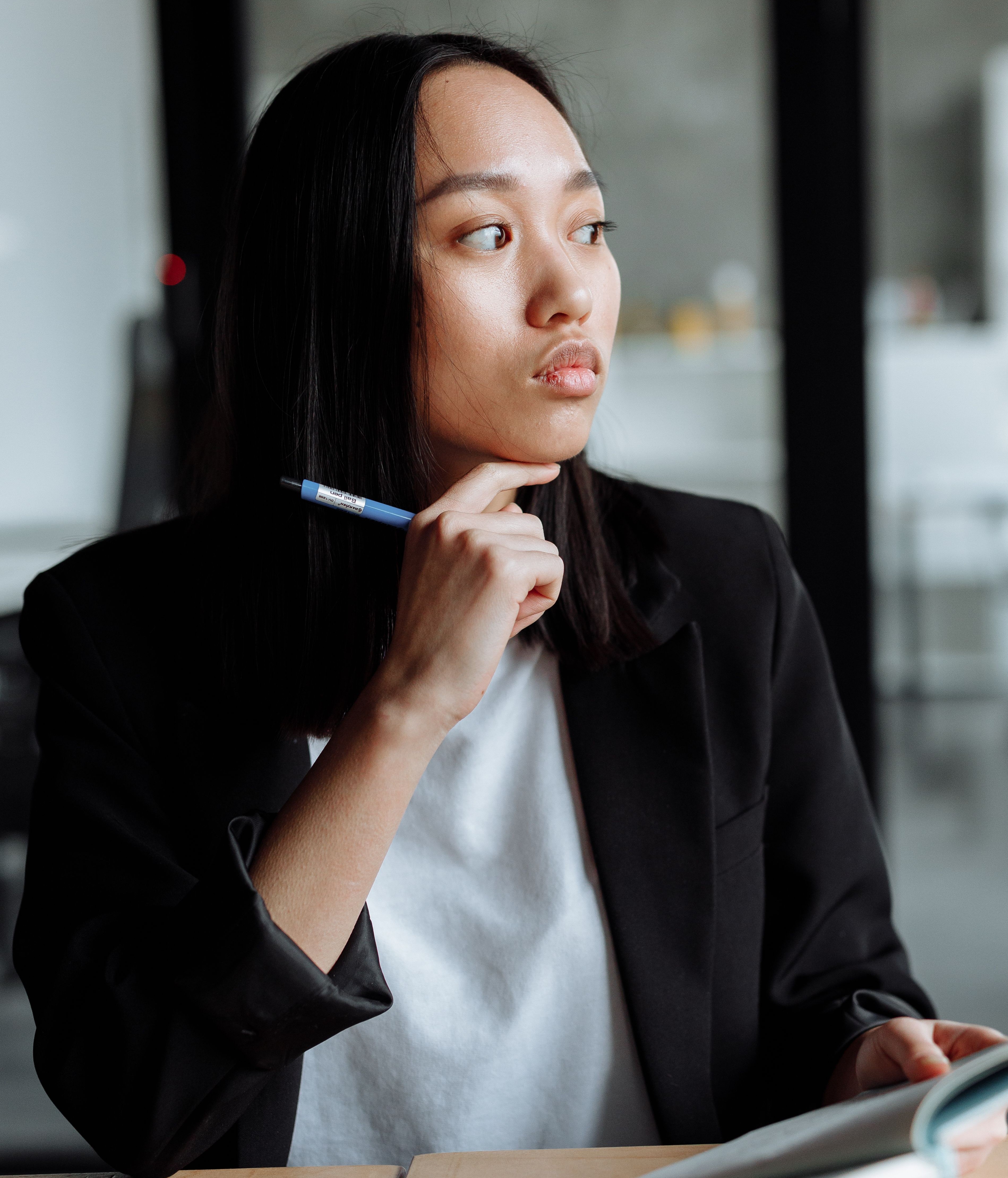 A thoughtful-looking woman holding a pen, reflecting on a boss gender biased situation A thoughtful-looking woman holding a pen, reflecting on a boss gender biased situation