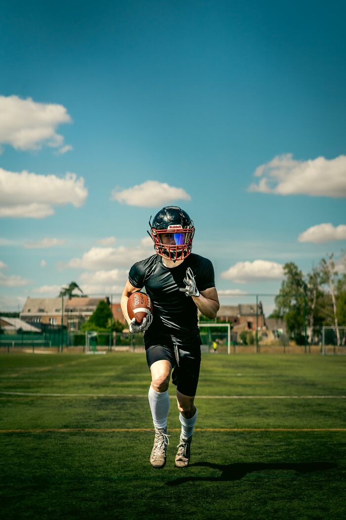 American football player running with a ball on a green field, showcasing common stereotypes about the US sports culture.