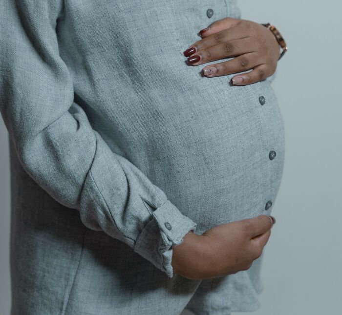 A pregnant person in a grey shirt cradling their belly, representing personal scandals or pregnancy issues.