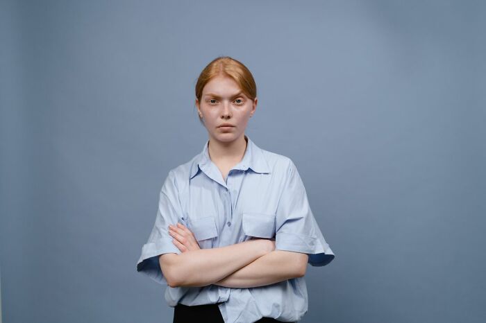 A young woman with an intense expression, arms crossed, embodying common US stereotypes.