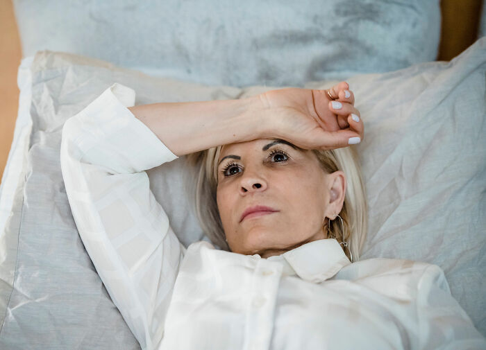 Woman in bed, holding her head, showing seemingly innocent health symptoms.