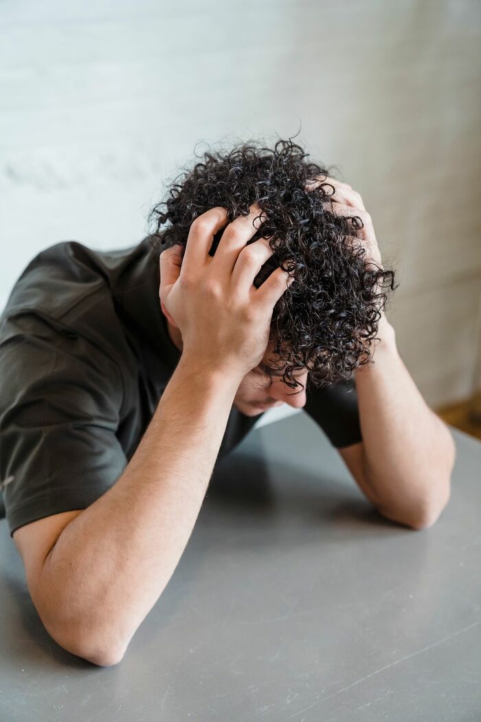 Man with curly hair grasping his head in frustration, awaiting a comforting dinner and hot tea.