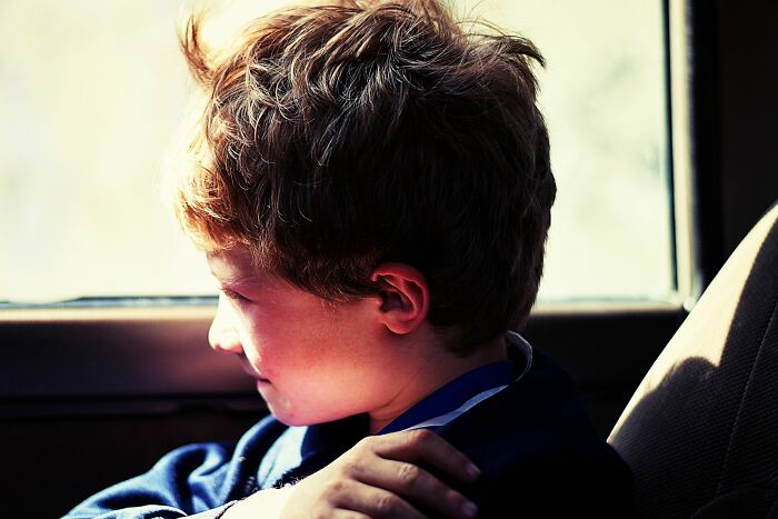 A young child with brown hair looking out a car window, with sunlight on their face.