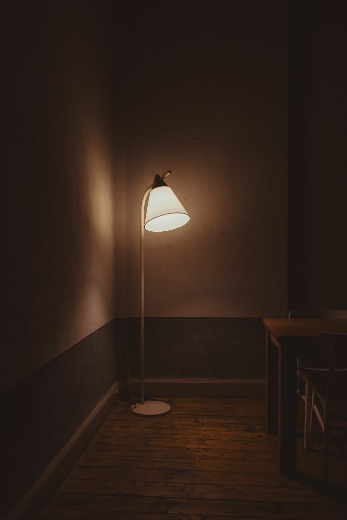 A dimly lit room with a single floor lamp providing light in a corner. Safety tips for women living alone.