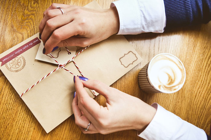 A person tying a string around a festive brown envelope, next to a cup of coffee. An act of petty revenge. A person tying a string around a festive brown envelope, next to a cup of coffee. An act of petty revenge.