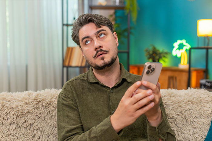Man holds a phone, looking up with a thoughtful expression, planning petty revenge for spam calls. Man holds a phone, looking up with a thoughtful expression, planning petty revenge for spam calls.
