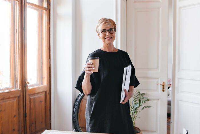 A smiling woman holding a coffee cup and documents, representing surprising things wealthy people buy.