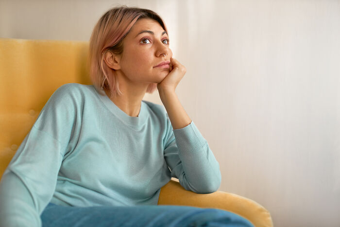 A woman with pink hair sitting in a yellow chair, deep in thought, about dating red flags.